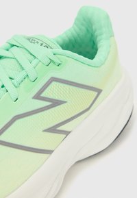 Light green athletic shoe with a textured upper, reflective gray logo, and white sole. Features lace-up design and cushioned collar.