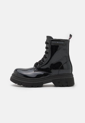 Botte noire brillante style combat avec semelle épaisse, lacets noirs, logo Tommy Hilfiger sur le côté et languette au talon.