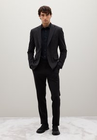 Abito nero slim fit, con rever a notched, chiusura a un bottone e camicia da sera nera abbinata. Tessuto liscio e pantaloni su misura.