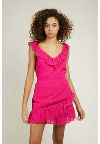 Robe rose à volants avec un décolleté en V, présentant des motifs ajourés et une jupe superposée. Le tissu semble léger et texturé.