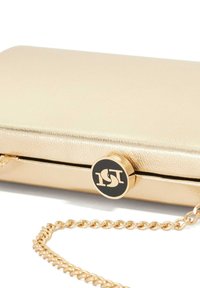 Gold clutch purse with a smooth metallic finish, featuring a chain strap and a round black and gold logo accent on the clasp.