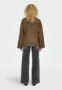 Brauner Oversize-Pullover mit weiten Ärmeln, kombiniert mit grauen Jeans im Schlagstil. Der Pullover hat eine glatte Textur, während die Hose einen verblassten Look aufweist.