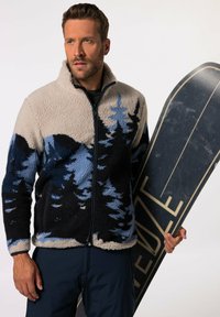 Fleecejakke med halv lynlås, i en farvesammensætning af creme, blå og sort, med et skovmønster. En snowboard holdes i den ene hånd.
