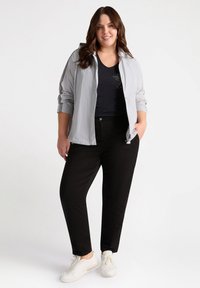 Ljusgrå zip-up jacka med huva, svart V-ringad tröja, svarta byxor och vita sneakers. Slät textur, avslappnad passform, subtila detaljer.