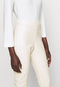 Jasnokremowe, wysokie spodnie wykonane z gładkiego, elastycznego materiału. Posiadają bezszwowy pas i dopasowany krój wzdłuż nóg.