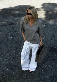 Pilkas V-nugaroje marškinėliai su trumpomis rankovėmis, balti plačios kojų kelnės ir tamsiai pilka rankinė. Lygi medžiaga, laisvas kirpimas ir minimalus aksesuarų kiekis.