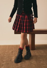 Plisovaná sukně v červené a černé barvě, doplněná černým cardiganem, černými kotníkovými botami a červenými volánkovými ponožkami.