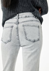 Grijze denim jeans met een vervaagde afwerking, voorzien van twee achterzakken en een middelhoge taille. De stof heeft een gladde, iets gestructureerde uitstraling.