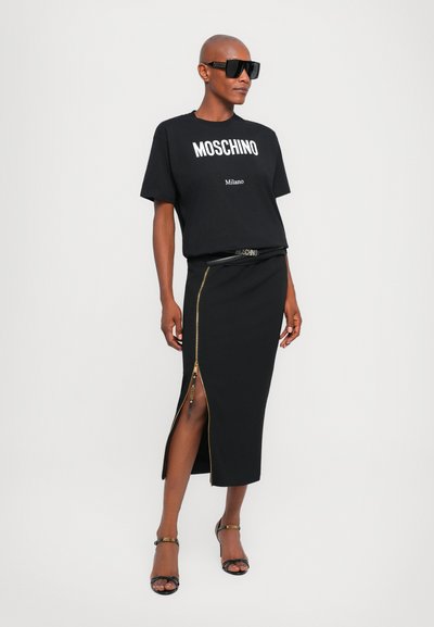 T-shirt noir Moschino avec logo blanc, jupe noire taille haute avec une fermeture zippée sur le côté, et sandales noires à lanières avec accents de logo.