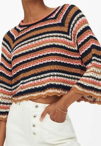 Skrócony sweter na szydełku z poziomymi paskami w kolorach granatowym, różowym, kremowym i brązowym. Dół z falbaniastym wykończeniem oraz szerokie rękawy.