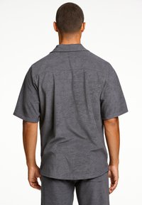 Camisa de manga corta gris con una textura suave, cuello tipo polo y corte relajado. Presenta un diseño simple y limpio, sin adornos.