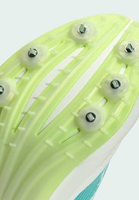 La suola delle scarpe da pista presenta una plastica leggera verde-gialla con accenti bianchi, sei punte metalliche e modelli di presa texture.
