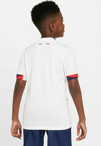 T-shirt de sport blanc avec un col rond, présentant des accents rouges et bleus sur les poignets. Design simple, tissu lisse et sans motifs visibles.