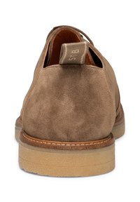 Scarpa slip-on in suede marrone con superficie texture, punta rotonda e suola in gomma spessa. Presenta un'etichetta a strappo decorata sul retro.