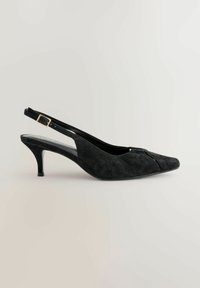 Černé semišové slingback boty na jehlovém podpatku s špičatou špičkou a malou zlatou sponou na pásku, umístěné na jednobarevném světlém pozadí.