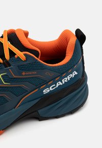 Pantof de exterior GORE-TEX, de culoare verde închis și negru, cu accente portocalii, suprafață din plasă texturată și logo vizibil pe lateral.