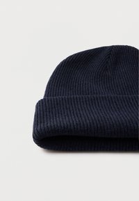 Tumši zilas krāsas ribu adījuma cepure ar atlocītu malu, raksturīga mīksta tekstūra un cieši pieguļošs dizains. Bez papildu dekorācijām.