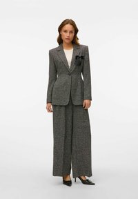 Halli tweed ülikond, millel on sobiv blazer ühe nupuga kinnitamine ja laiad püksid. Blazerit kaunistab must lips.