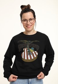 Sudadera negra con un gráfico de guitarra y franjas rojas, blancas y azules. El diseño incluye un águila y el texto "Lynyrd Skynyrd".