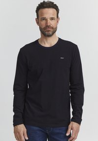 Hosszú ujjú, sötétkék póló, kerek nyakkal, pamutból készült, kis, színes logóval a mellrészen. Egyszerű dizájn és szabás.