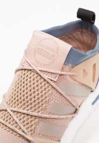 Scarpa atletica rosa chiaro con tomaia in mesh, dettagli rinforzati e collo rosa e blu. Presenta tessuto texturizzato e marchio distintivo.