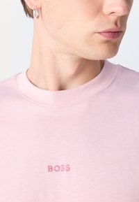 T-shirt en coton rose avec un col rond. Présente un logo "BOSS" brodé en rose assorti, mettant en valeur une texture lisse.