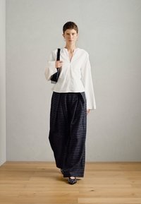 Bijela bluzica dugih rukava s V-izrezom, uparena s labavim crnim kariranim hlačama. Crna torba i cipele s posebnim uzorkom upotpunjuju ovu kombinaciju.