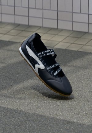 Fekete sportcipő fehér részletekkel, feltűnő elasztikus pántokkal, amelyeken a „REPLAY” márkajelzés látható, texturált talppal, minimalista dizájn.