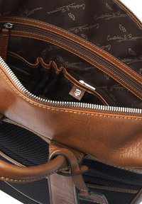 Brown leather bag interior showing a zip compartment and multiple pockets with a dark fabric lining featuring repeated logo pattern.