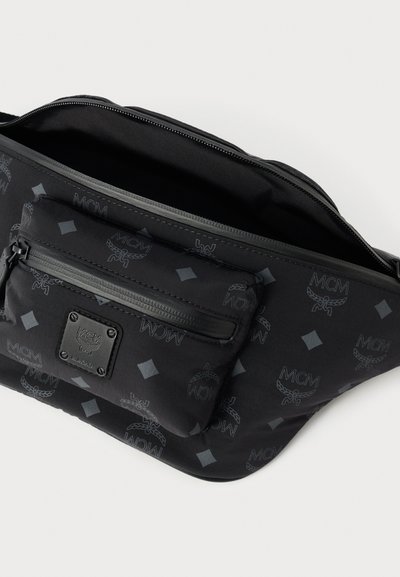 Bolsa de cintura preta da MCM com bolso frontal com fecho de correr, padrão de logótipo da marca e compartimento principal aberto sobre fundo branco.