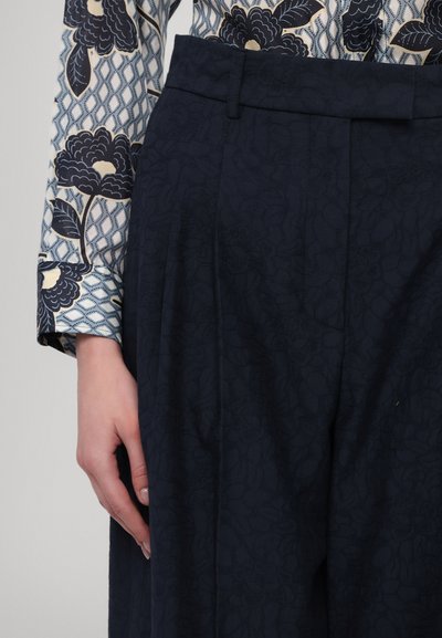 Marineblaue, gemusterte Hose mit Falten am Bund, kombiniert mit einer Bluse mit floralen und geometrischen Designs.