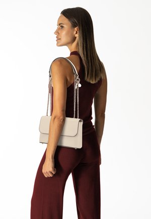 Sac à main en cuir beige avec une forme structurée, comportant des chaînes en argent et une fermeture à rabat. Texture lisse avec des bords noirs contrastants.