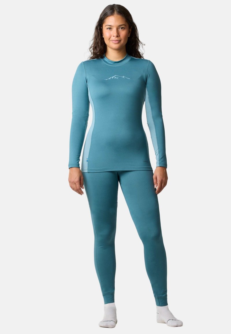 Long-sleeve, form-fitting base layer set in teal, features a mountain graphic. Smooth texture with seamless design, includes matching leggings.