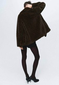 Cappotto in pelliccia finta con stampa leopardo marrone e colletto ampio, indossato sopra un mini vestito scuro e collant, abbinato a scarpe con tacco alto nere.