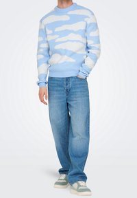 Lichtblauwe trui met witte wolkenpatronen; geribde manchetten en zoom. Gecombineerd met lichtblauwe jeans met een losse pasvorm en grijs-witte sneakers.