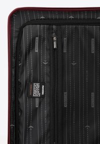 Red suitcase interior with a black lining. Features include a zipper, mesh pockets, and a label. Pattern includes gray stripes and airplane icons.