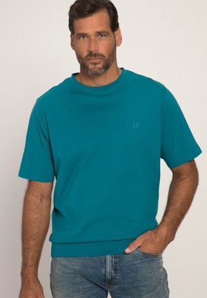 Türkisfarbendes Baumwoll-T-Shirt mit kurzen Ärmeln, Rundhalsausschnitt und lockerem Schnitt. Dezentes "JP"-Logo in der gleichen Farbe auf der Brust. Kombiniert mit blauen Jeans.