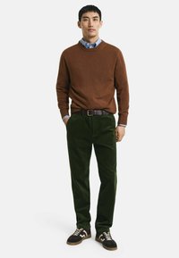 Brauner Strickpullover, hellblaues Hemd mit Kragen, dunkelgrüne Cordhose und schwarze Sneaker mit cremefarbenen Akzenten. Schlichte, taillierte Passform.