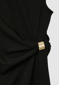 Robe noire avec un détail noué sur le côté, agrémentée d'un accent métallique doré. Le tissu est lisse, avec une coupe élégante et ajustée.