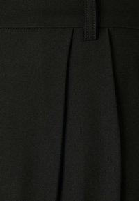 Černé kalhoty na míru s strukturovaným pasem a předními záhyby, vyrobené z texturované tkaniny s hladkým povrchem.