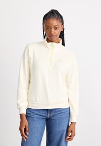 Cream fleece pullover with a high collar and half zipper in neon green. Features ribbed cuffs and waistband. Small logo on chest.