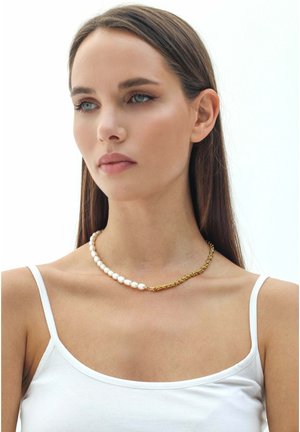 Collier de perles avec une chaîne en or, présentant des perles blanches disposées selon un motif en gradation. Le design marie harmonieusement les matériaux et les textures.
