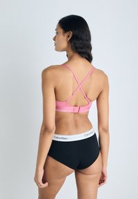 Modra ženska modrček Calvin Klein v roza barvi z zasnovo križnega traku; ujemajoči se črni kratki bokserji z belim elastičnim pasom z logotipom. Gladek, raztegljiv material.