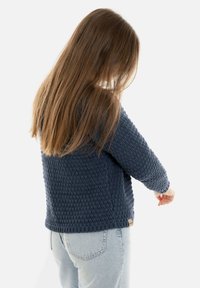 Marineblauwe gebreide trui met textuurpatroon, lange mouwen en een ronde halslijn. Draag met lichtgekleurde denim jeans, met de achterkant in beeld.