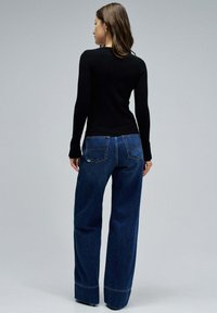 Haut noir à manches longues associé à un jean large bleu. Le jean présente une coupe classique, deux poches arrière et un ourlet légèrement effiloché.