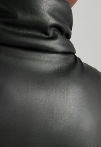 Musta nahkakangas, jossa on sileä rakenne ja hienovaraisia ryppyjä, esittelee kauniisti laskeutuvan muotoilun kauluksen ympärillä.