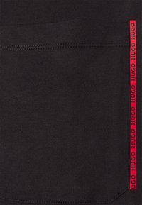 Tessuto nero con una finitura liscia presenta una prominente striscia verticale rossa etichettata "HUGO" ripetutamente lungo il lato.