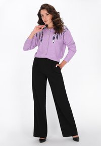 Cárdigan de punto lila con diseño de plumas de lentejuelas, cierre de botones, combinado con pantalones de pierna ancha negros de cintura alta y tacones negros.