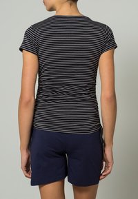 T-shirt de algodão riscado em preto e cinza, design ajustado com mangas curtas, emparelhado com calções azul-marinho, vista traseira mostrando detalhe franzido.