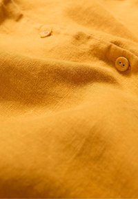 Yellow linen fabric with a textured surface, featuring two button details. The material appears lightweight and slightly crumpled.